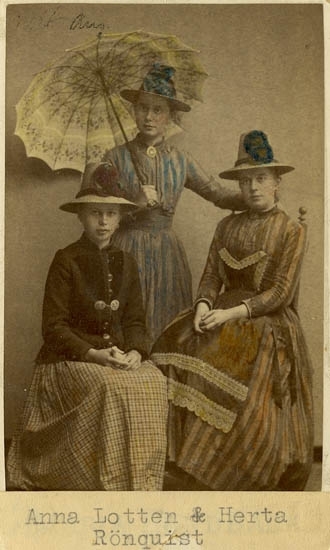 kolorerat svartvitt foto. Tre tonårsflickor. Två sitter och en står i mitten. Flickan i mitten håller i ett kinesiskt parasoll. 